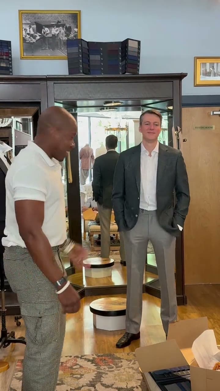 In the Raleigh shop, the groom stands in a green-grey sport coat and grey trousers while the tailor, in a white polo, looks over the fit