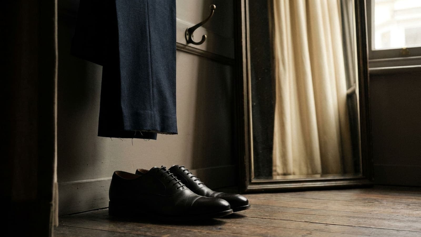 Polished dark oxford shoes on a fitting room floor beneath trousers with an unfinished hem